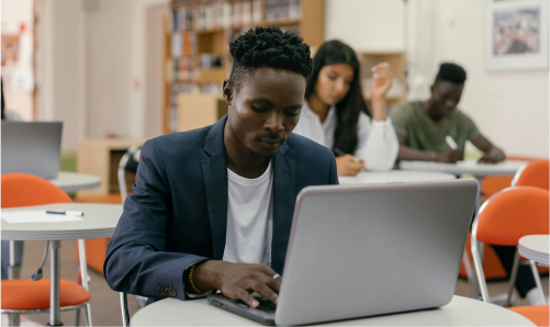 Student using a laptop in a classroom while others study in the background.